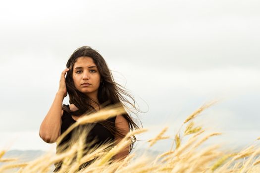 A contemplative woman standing in a windy field in Masyaf, Syria, captured in a moody atmosphere.