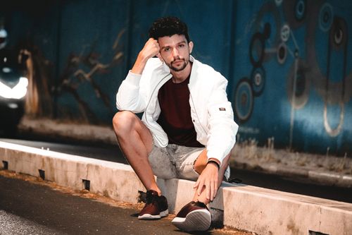 Free A fashionable man in a white jacket and denim shorts poses on an urban street, expressing contemporary style. Stock Photo