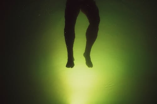 Anonymous man swimming in water near green background