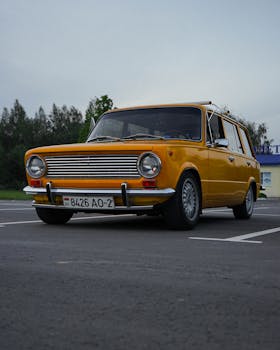 Yellow vintage station wagon parked on asphalt road with trees in the background.