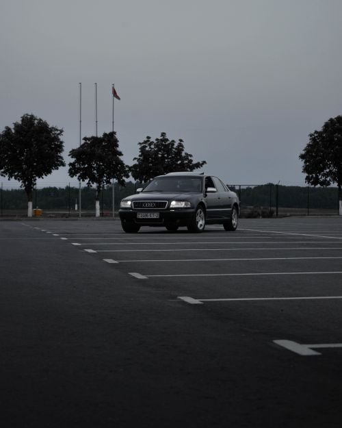 Free A stylish sedan parked in a deserted parking lot with trees in the background, captured at dusk. Stock Photo