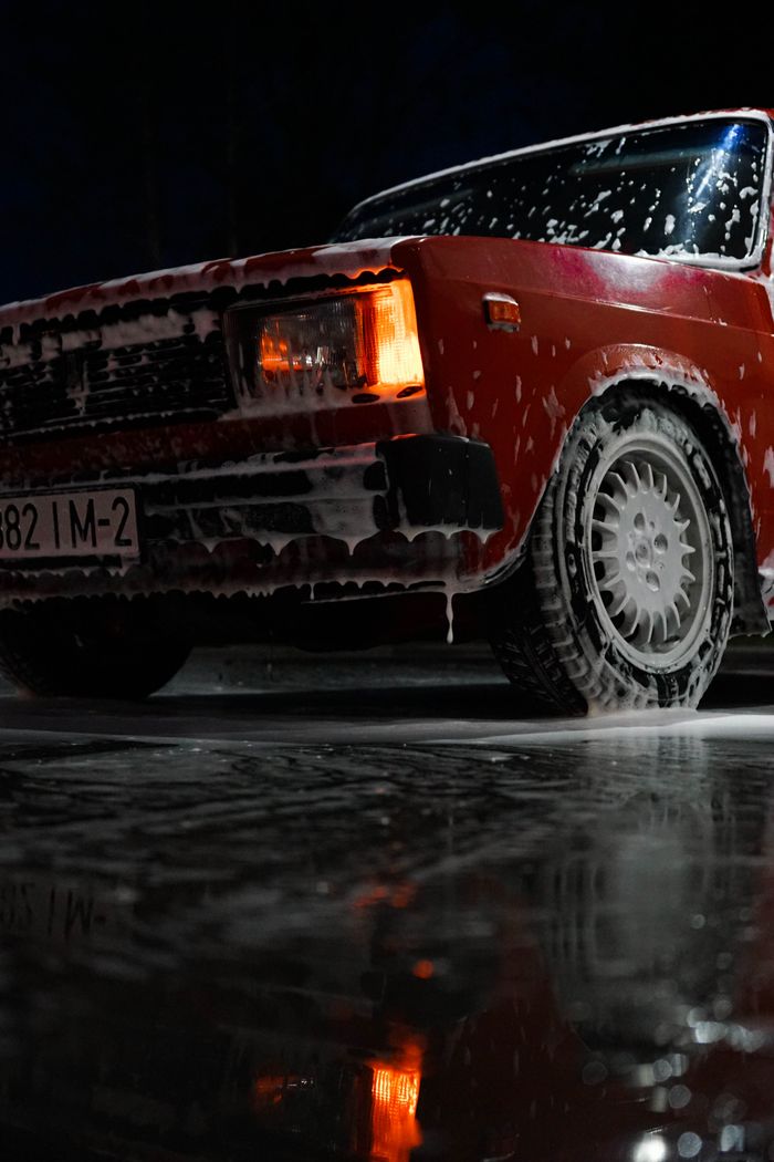 Red car soaked in soap suds at the wash bay