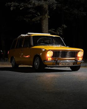 Classic yellow station wagon with headlights on in the dark.