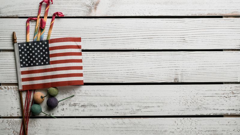 A close-up of an American flag with fireworks on a rustic wooden surface, symbolizing patriotism and celebration.