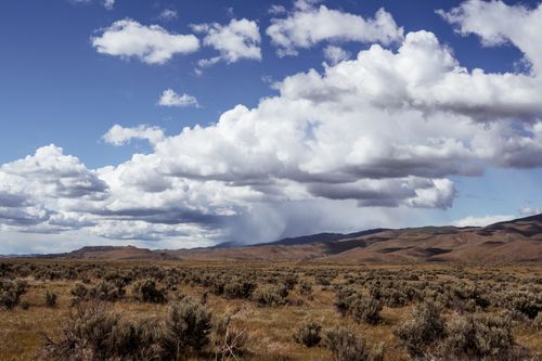 Free Vast field with dramatic clouds over barren mountains, capturing nature's serene beauty. Stock Photo