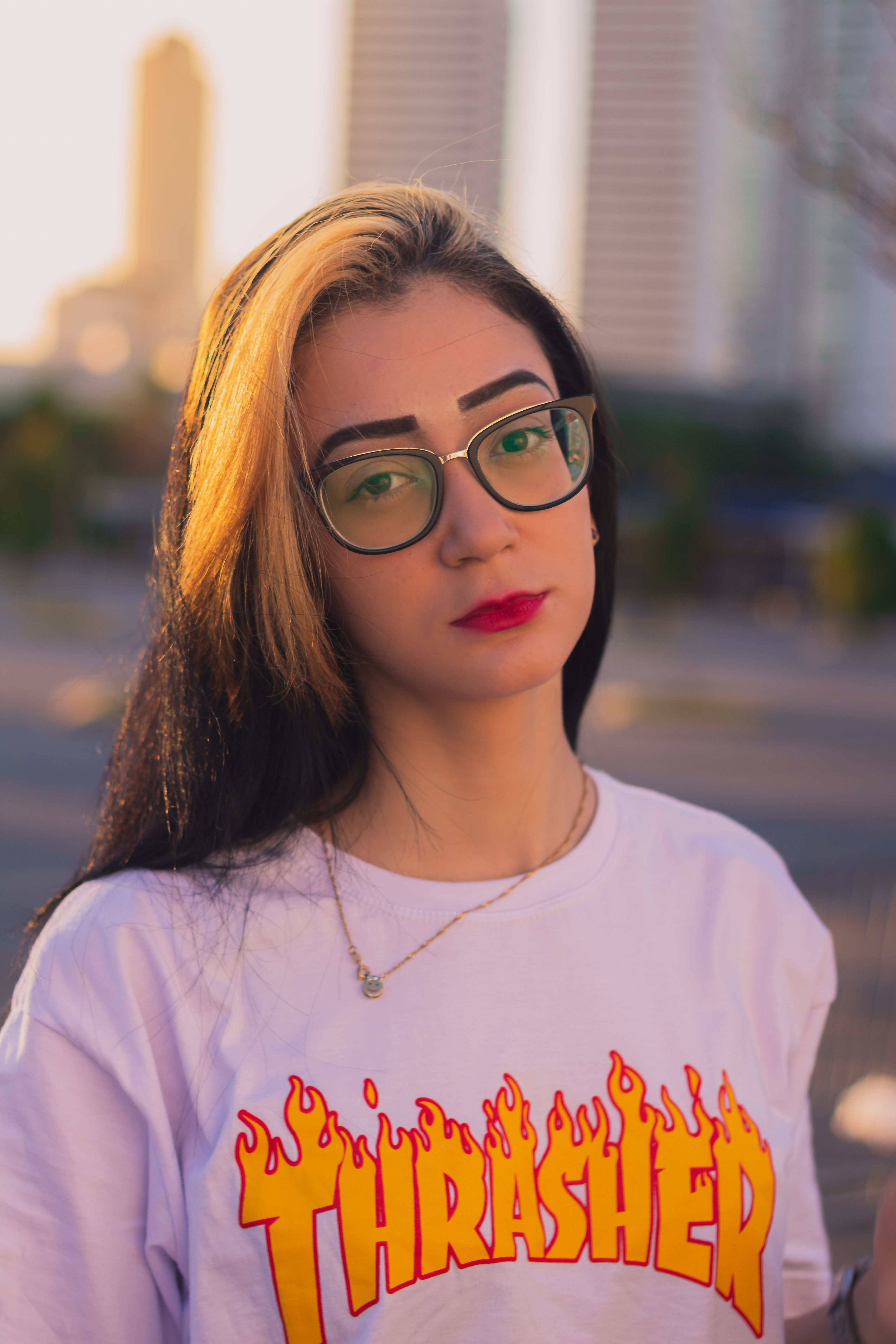 Portrait of a fashionable woman with glasses and blonde highlights outdoors at sunset.