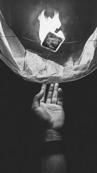 一张迷人的黑白图像，展示了一只手正在释放燃烧的纸质天灯