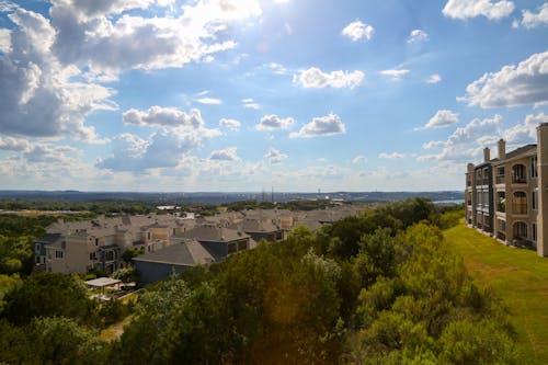 Modern multi storey buildings surrounded by tall verdant trees in park under light blue sky with clouds