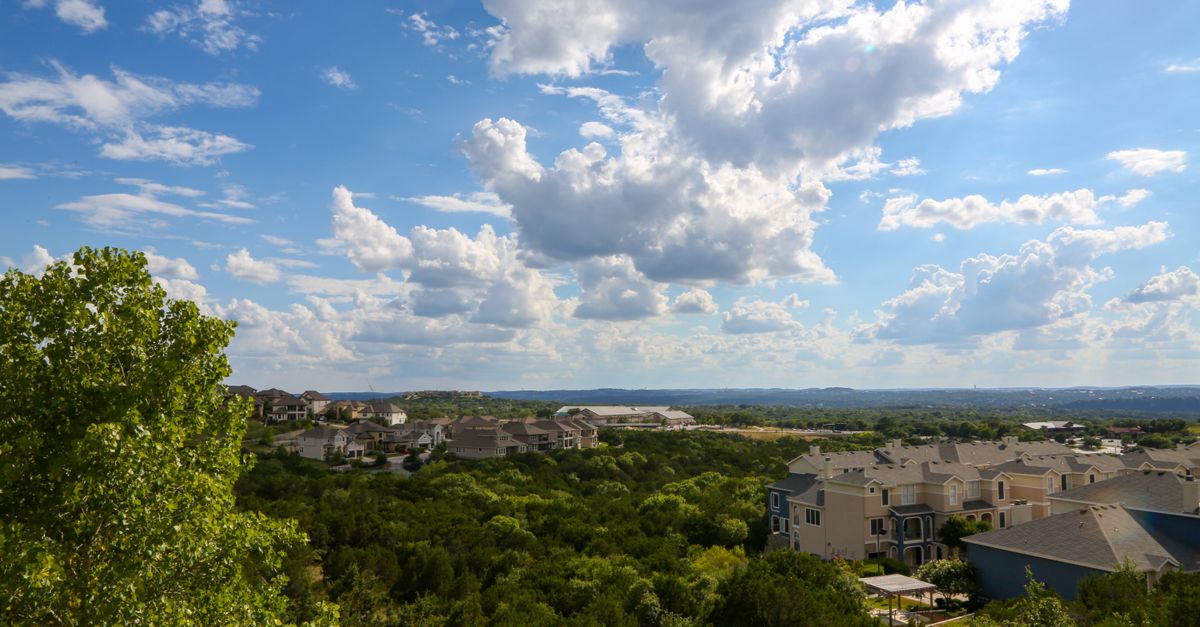 Modern constructions surrounded by vibrant green trees under light blue sky covered with dense clouds in sunlight