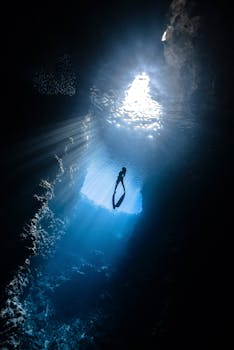 A breathtaking view of a scuba diver silhouetted in a sunlit underwater cavern.