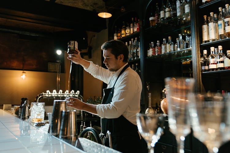 Man In White Long Sleeve Shirt Pouring Wine On Clear Wine Glass