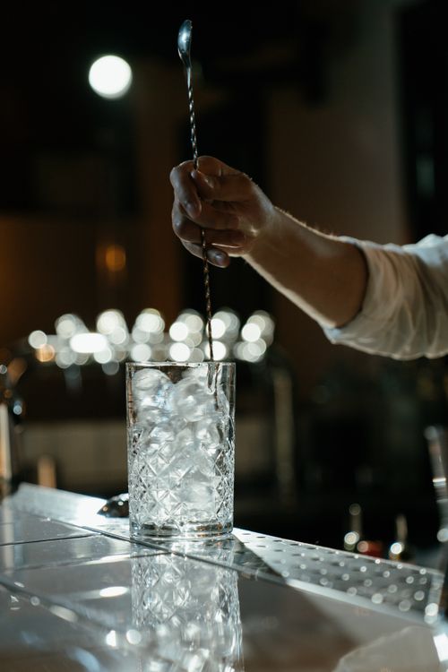 Free Close-up of bartender stirring ice in a glass with a bar spoon, creating a refreshing cocktail. Stock Photo
