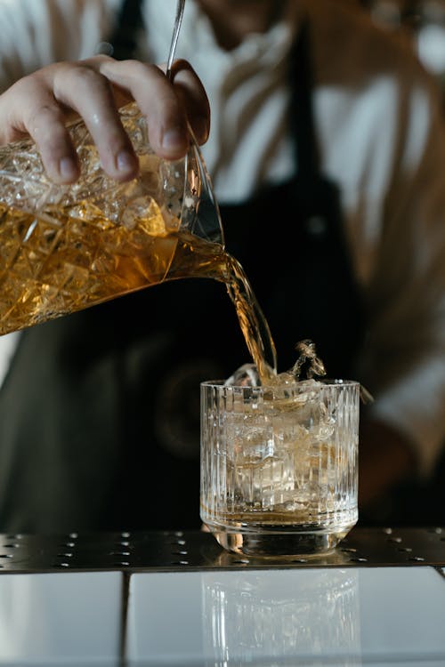 Person Pouring Brown Liquid on Clear Drinking Glass