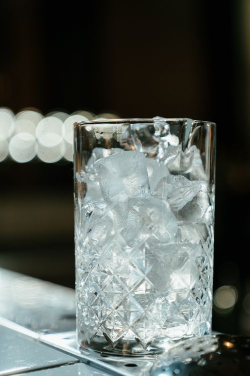 Free Elegant crystal glass filled with ice cubes on a bar counter with a blurred background. Stock Photo