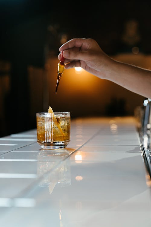 Person Holding a Pen and a Shot Glass With Yellow Liquid