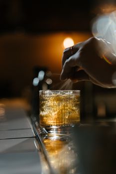 在昏暗的酒吧氛围中，一只手正熟练而热情地装饰着威士忌鸡尾酒