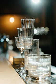 Elegant arrangement of empty cocktail and champagne glasses on a bar counter with blurred background lights.