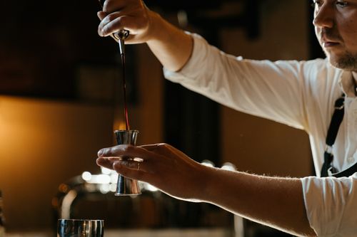 Free A bartender in a uniform expertly measures spirits with a jigger in a dimly lit indoor bar setting. Stock Photo