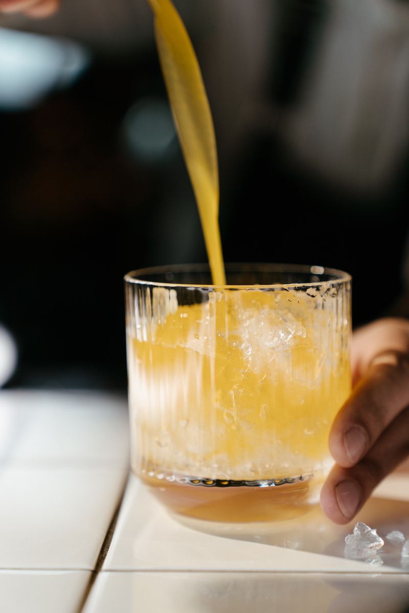 Segelas jamu kunyit asam berwarna kuning cerah dengan irisan kunyit segar