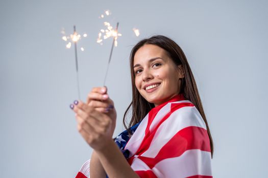 一位年轻女子身披美国国旗，用烟花庆祝独立日