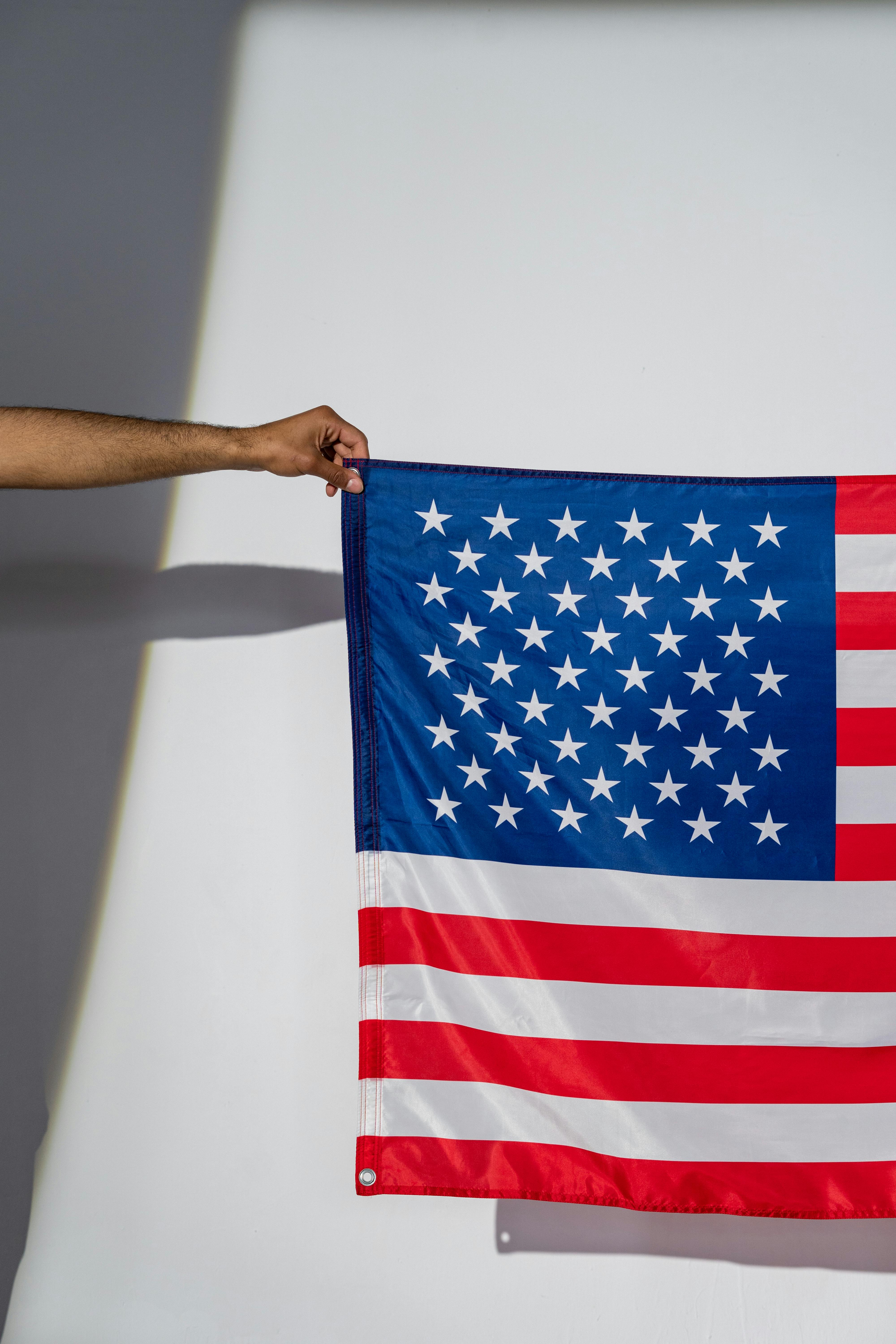 A person holds an American flag against a plain white background, symbolizing patriotism.