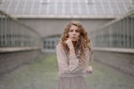 一个卷发的年轻女子在模糊的建筑背景下若有所思地在户外摆姿势