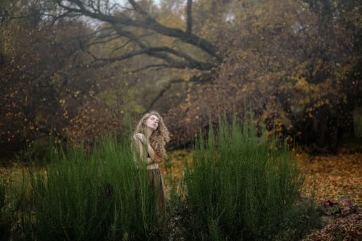 一名妇女闭着眼睛，站在秋叶环绕、植物高大的郁郁葱葱森林中