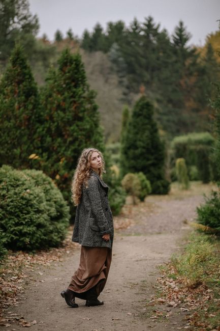 A woman with curly hair walking on a forest path surrounded by autumn foliage, exuding tranquility.