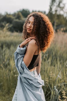 一位卷发的时尚女性在田野里摆着姿势，享受夏日的户外活动