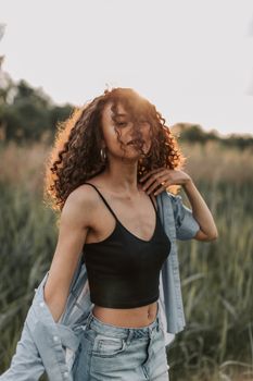 一位卷发的年轻女子穿着休闲时尚的服装，在户外享受着阳光明媚的一天