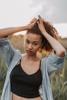 日落时分，一位卷发的时尚年轻女子在田野里摆姿势，展现出现代时尚与自然之美