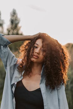 日落时分，一名卷发女子身着休闲装，在户外摆着姿势