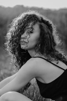 黑白照片中，一位留着卷发的时尚年轻女子站在户外