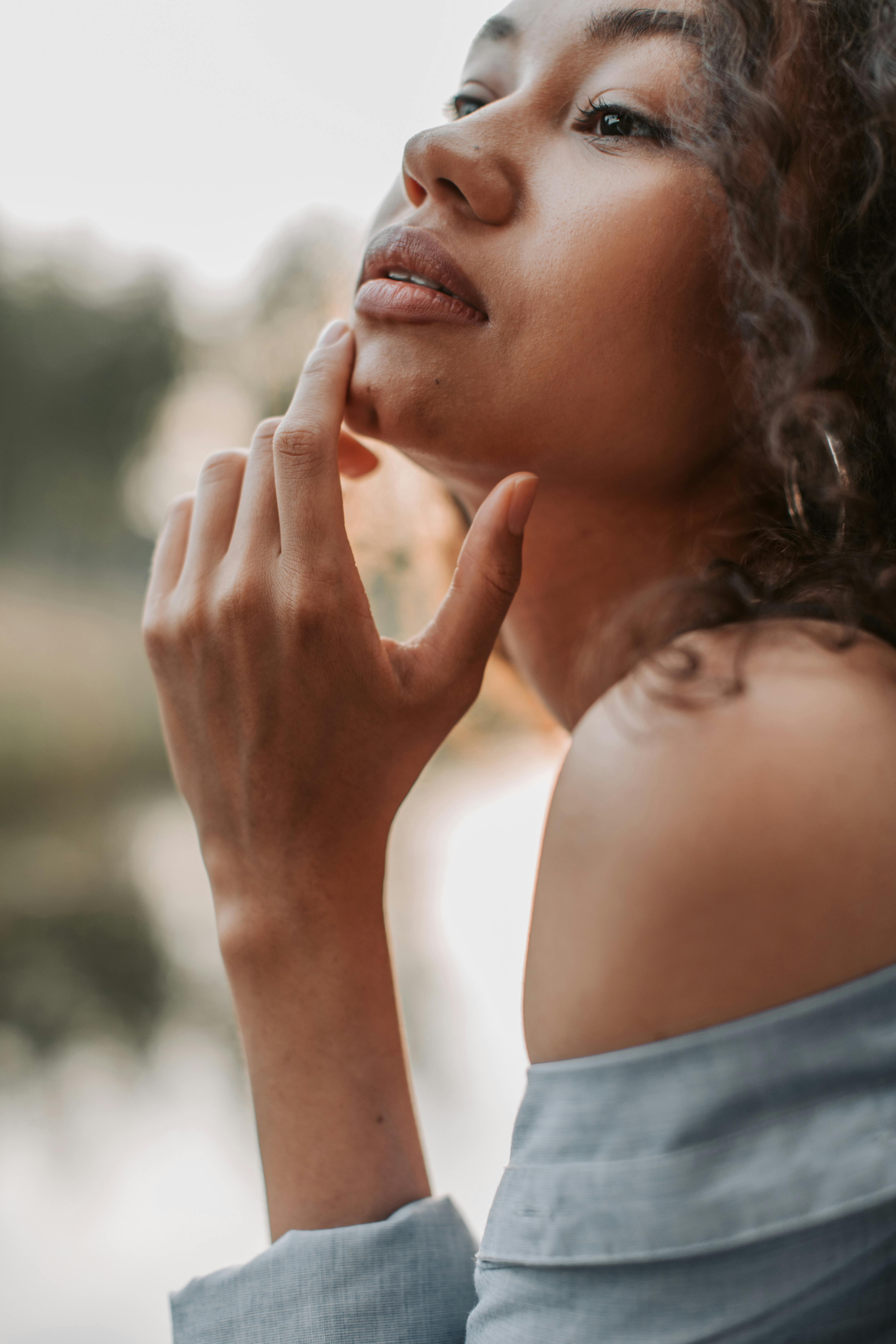Close-up portrait of a woman with curly hair posing thoughtfully outdoors.