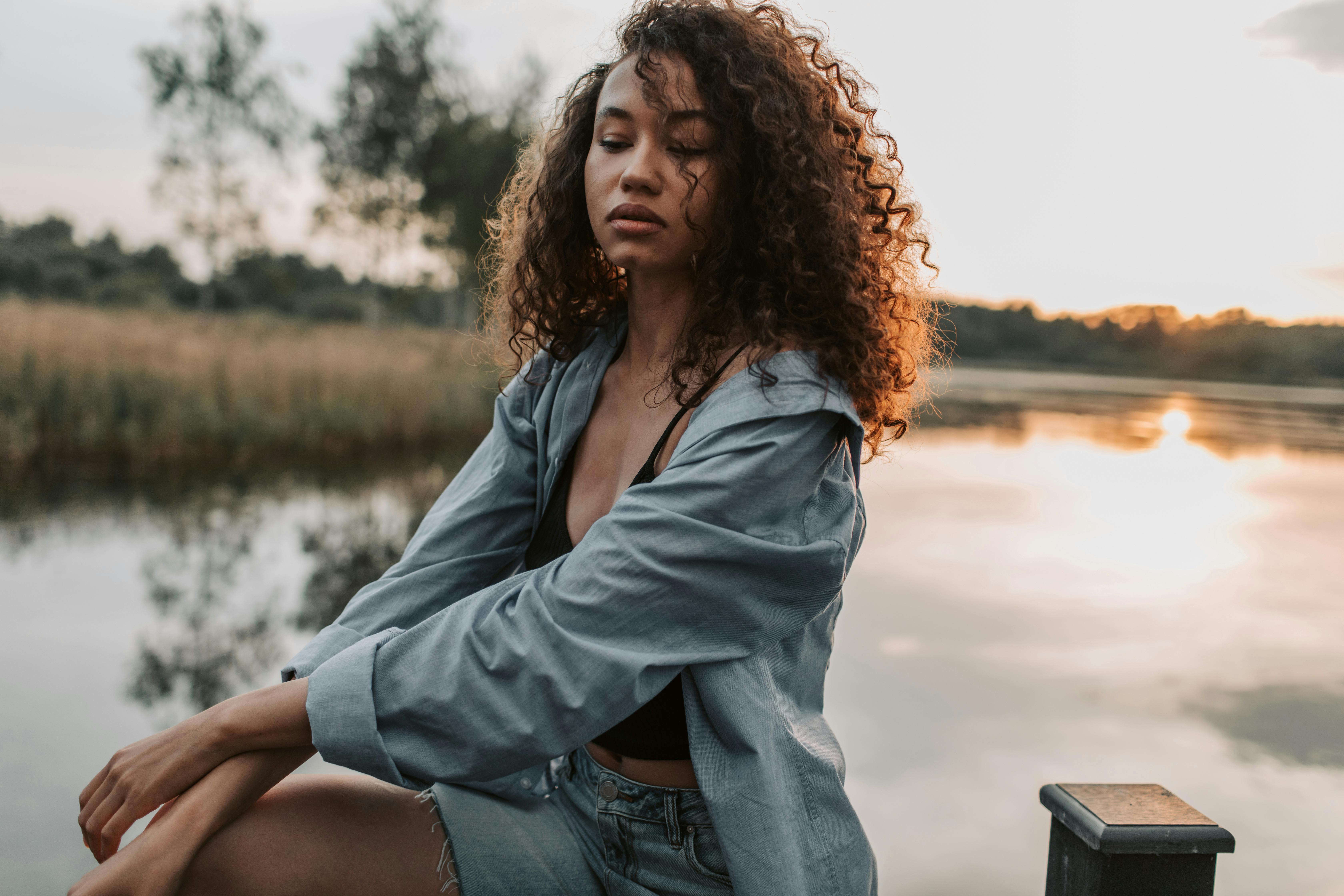 在日落时分，一个留着卷发的时尚女人在宁静的湖边摆姿势的坦率镜头