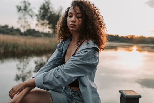 日落时分，一位卷发时尚女子在宁静的湖畔摆姿势，被坦率地拍摄下来