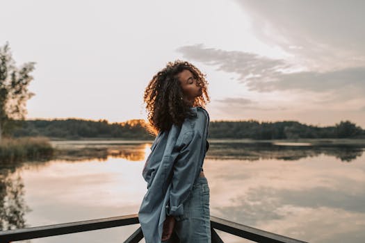 一位卷发优雅的女子在日落时分的宁静湖畔，展现出风格与宁静