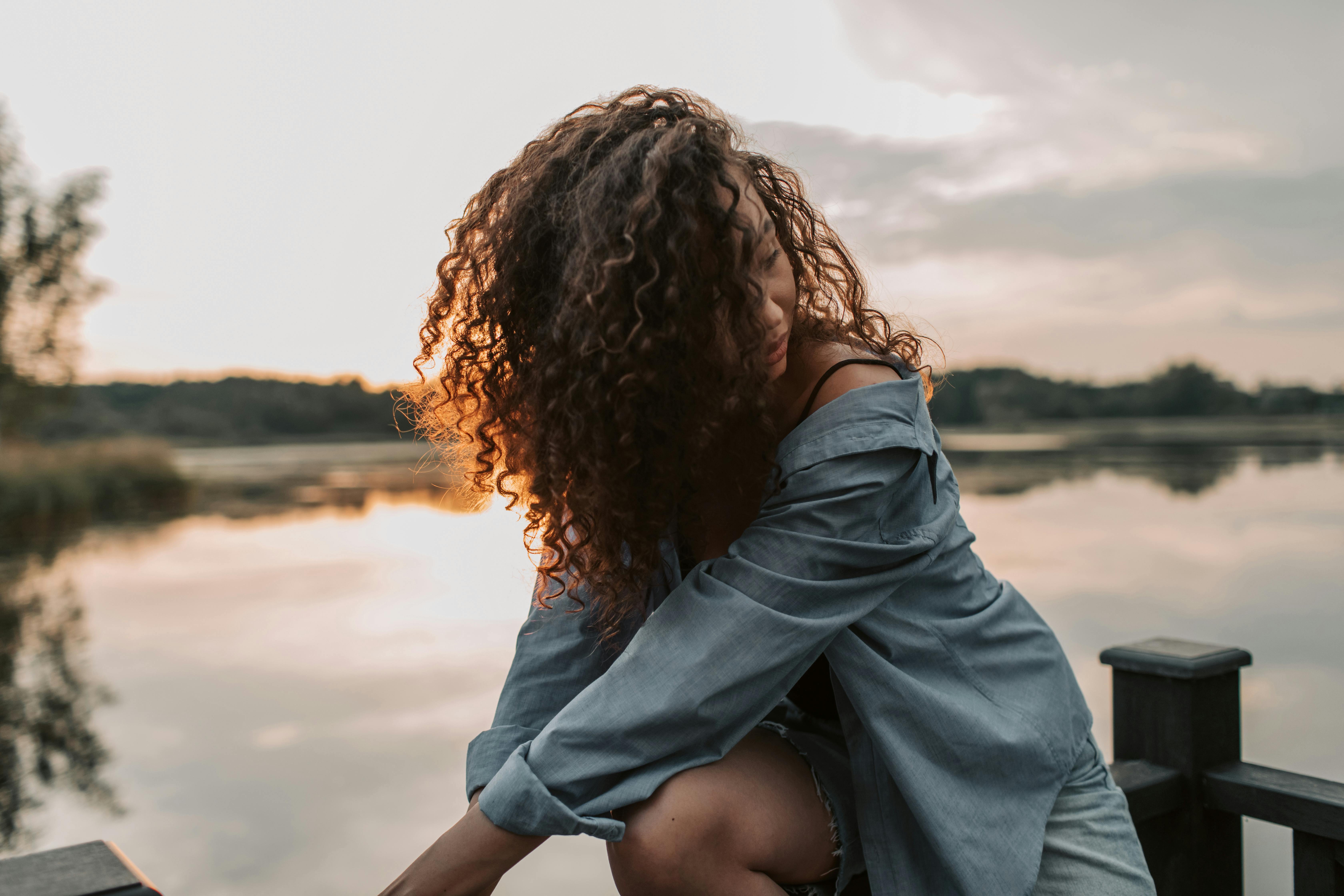 一个卷发的女人在日落时在湖边摆姿势，散发着美丽和宁静
