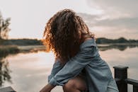 一个卷发的女人在日落时在湖边摆姿势，散发着美丽和宁静