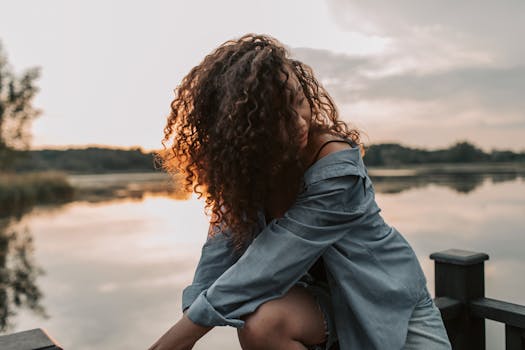 日落时分，一位卷发女子在湖边摆着姿势，美丽而宁静