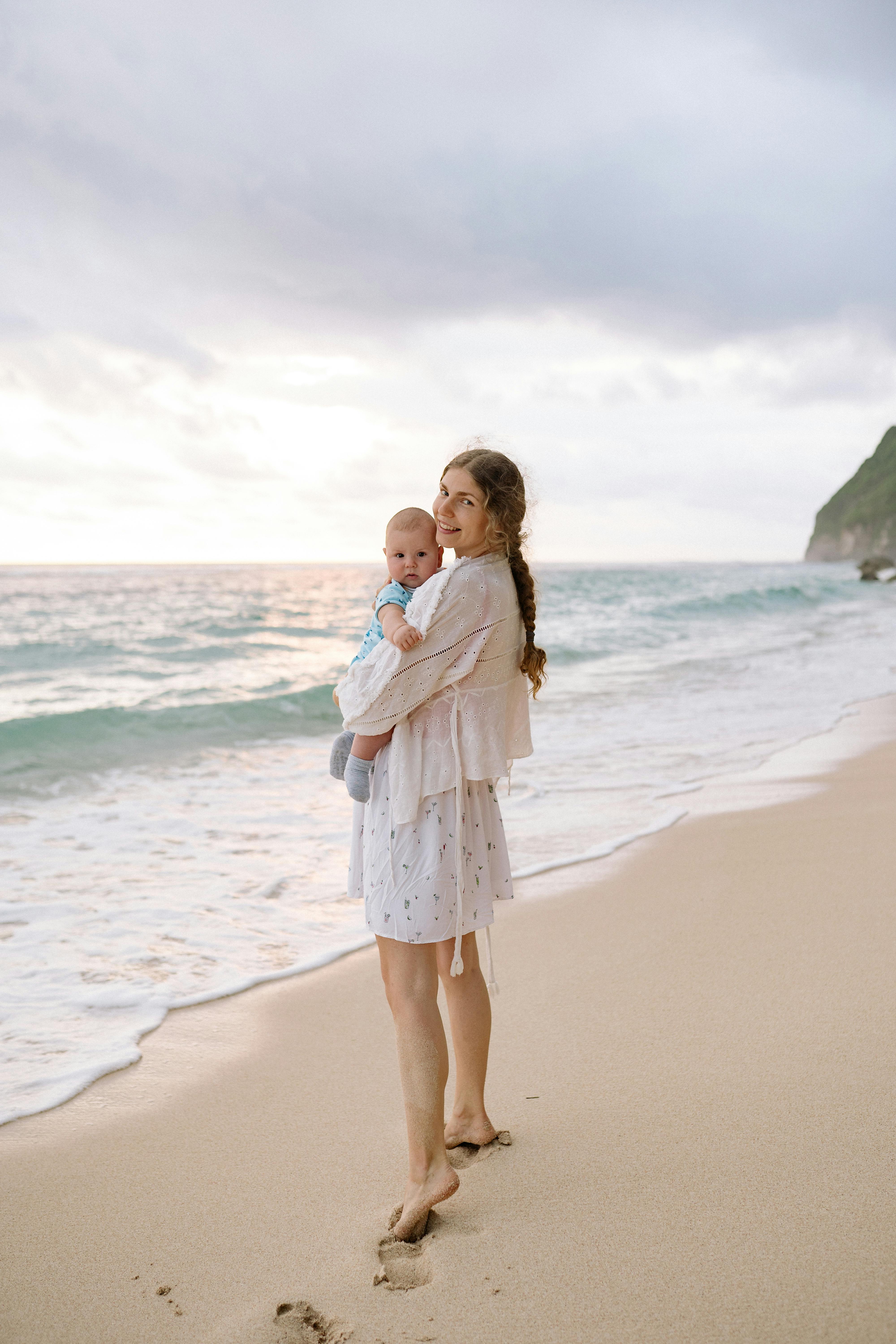 一位母亲抱着她的男婴，在沙滩上享受海边宁静的日落