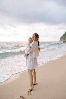 一位母亲抱着她的男婴，在沙滩上享受海边宁静的日落