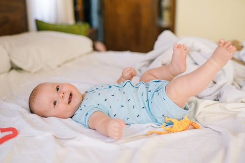 Free Adorable baby in blue onesie lying on bed with toy dinosaur, smiling brightly. Stock Photo