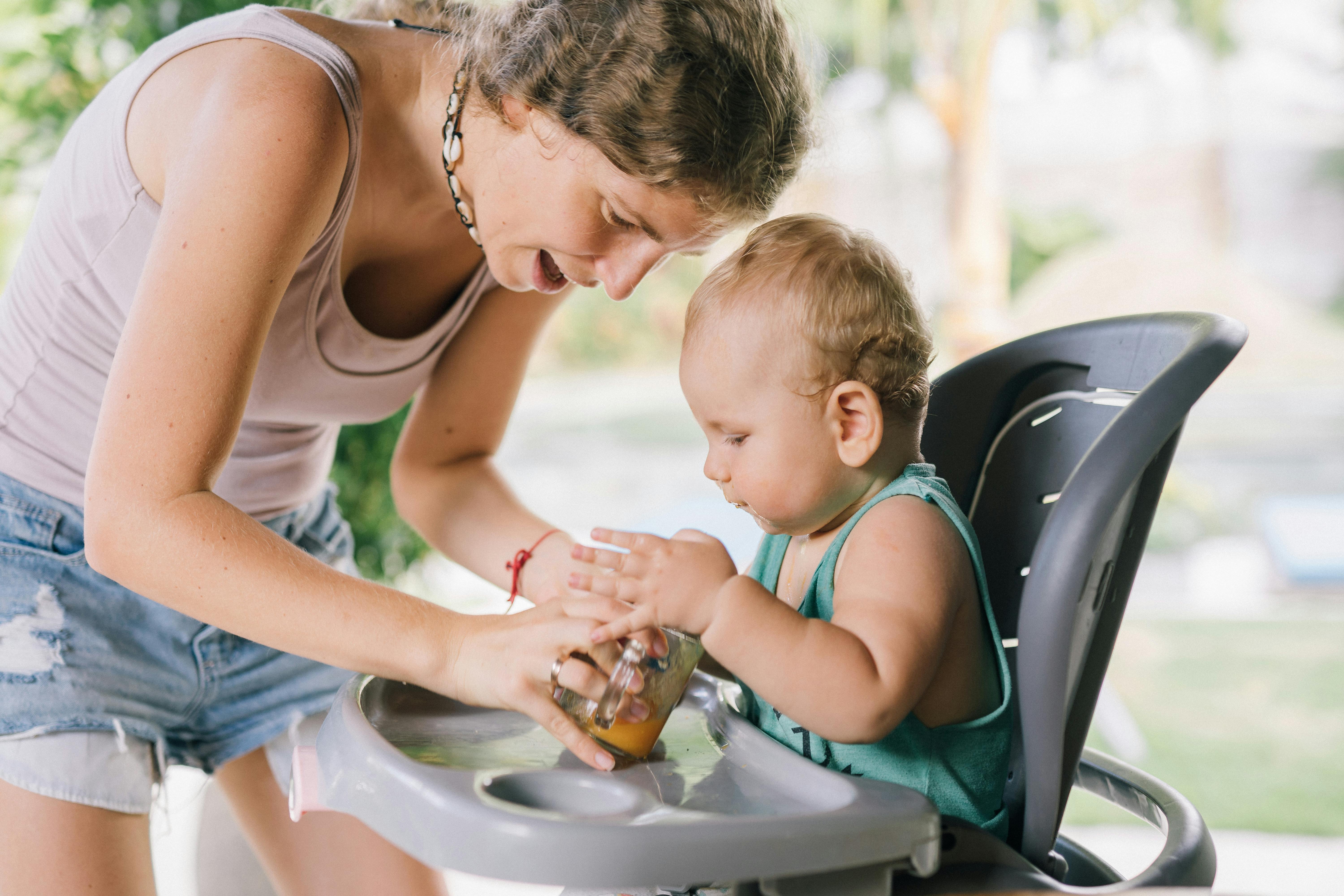A mother lovingly feeds her baby in a high chair outdoors, showcasing familial bonding and care.