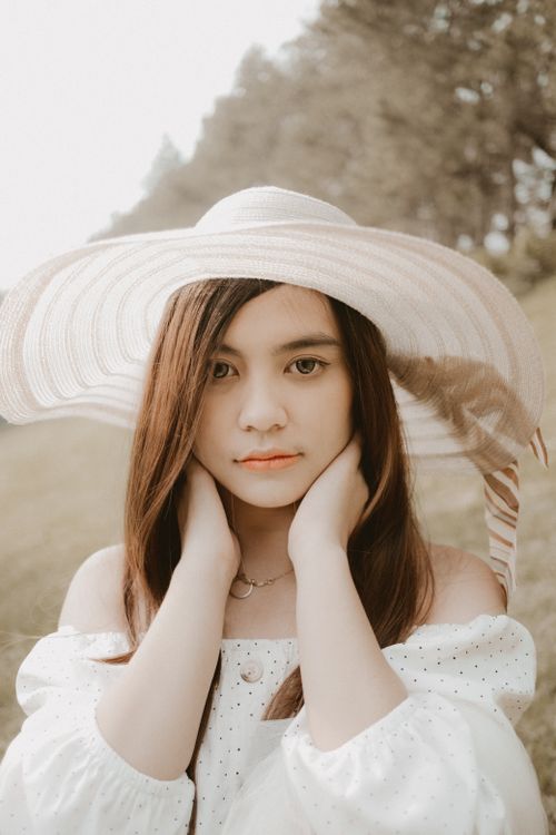 Free A thoughtful woman with a sun hat posing in a serene outdoor setting, showcasing elegance and fashion. Stock Photo