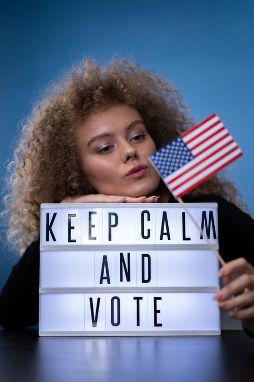 Free Woman with curly hair holding American flag, promoting voting with text sign. Stock Photo