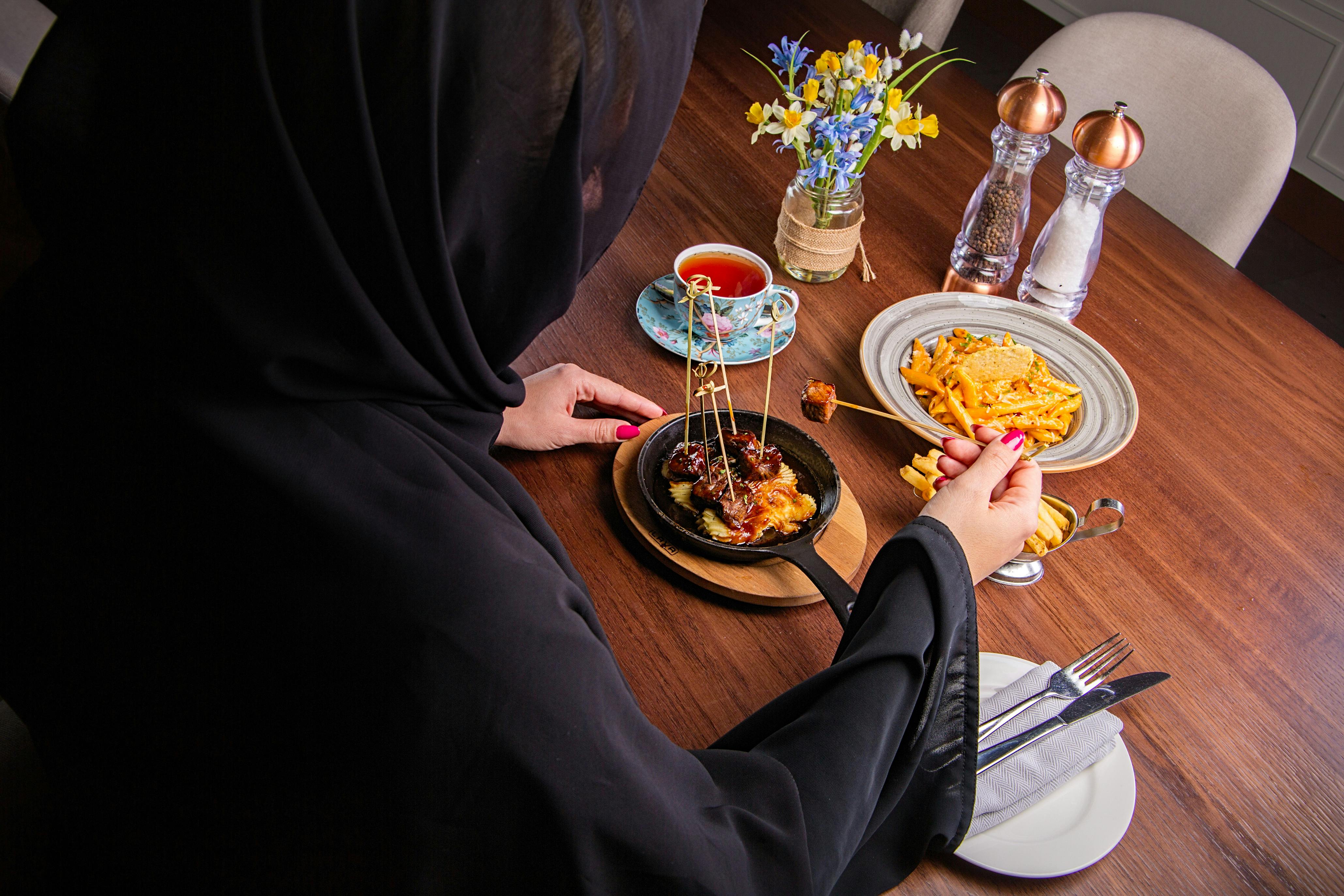 A Muslim woman enjoys a meal at a Dubai restaurant. Featuring delicious food and a warm ambiance.