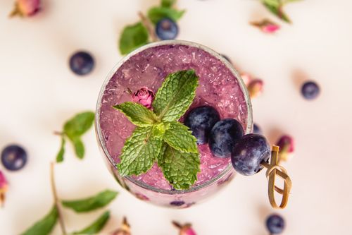 Free Refreshing beverage with blueberries, mint, and rose petals served on crushed ice, perfect for a warm day. Stock Photo