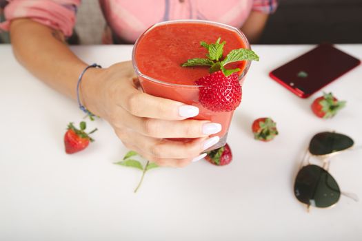 Hand holding a refreshing strawberry smoothie with fresh mint in a Dubai cafe. Perfect summer treat.