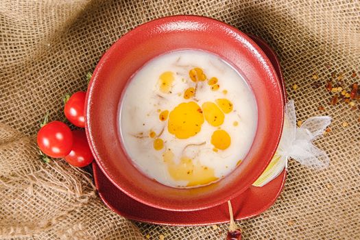 Top view of creamy red lentil soup with tomatoes and olive oil in a red ceramic bowl on a burlap background.